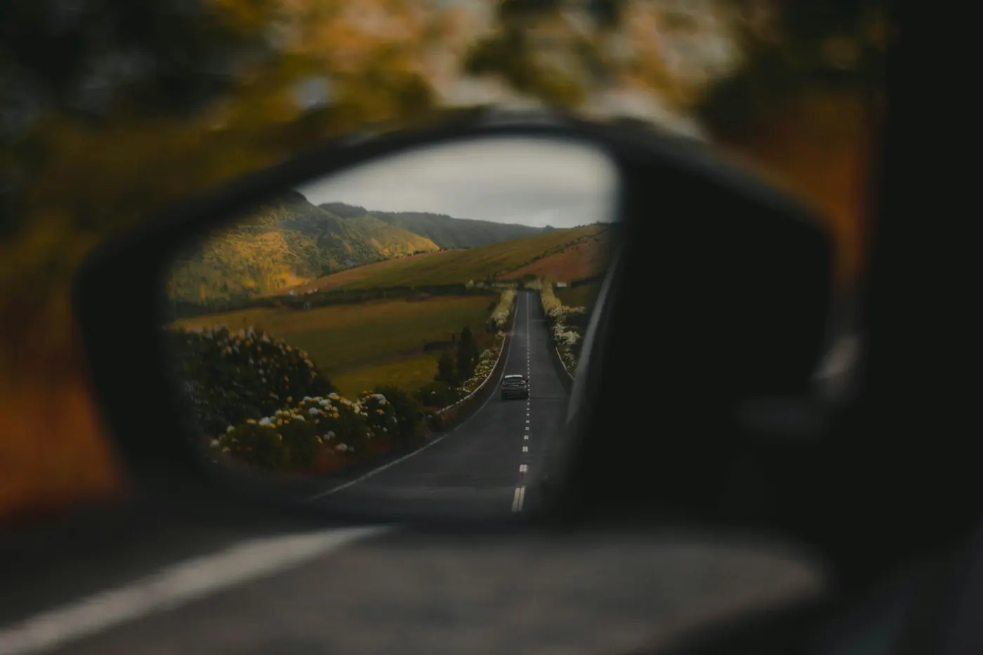 Een zijspiegel die een landweg met bomen weerspiegelt